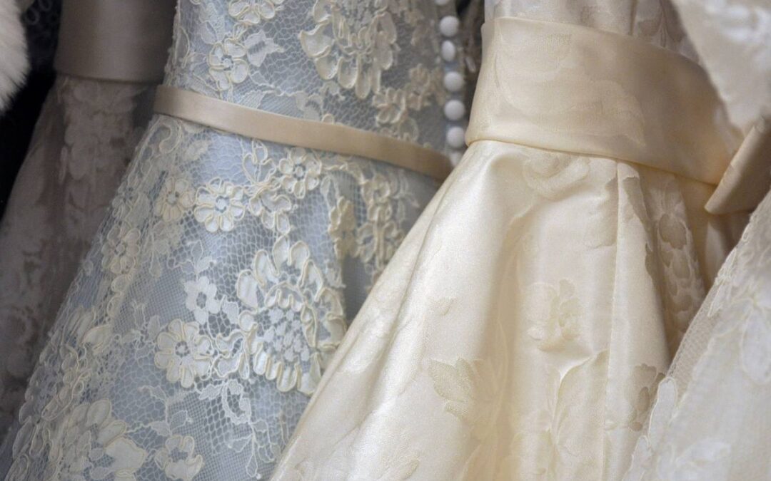 Close-up of two elegant bridal dresses with intricate lace detail and a satin ribbon.